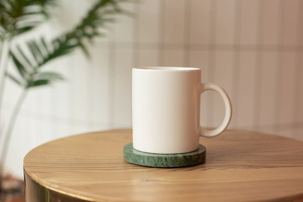 White ceramic mug on a wooden table next to a plant